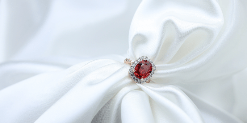 Ruby ring with diamonds on gold ring setting with white satin background
